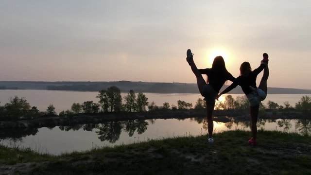Athletic young women are doing dancer pose, yoga on a shore of a river, 4k