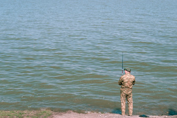 adult man in camouflage fishing on the beach. A real angler catches fish on a sunny day. professional fisherman casts a fishing rod