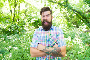 Naklejka na ściany i meble Tipping a wink. Caucasian man on summer landscape. Bearded man with unshaven beard hair on caucasian face. Caucasian european guy keeping arms crossed outdoor. Caucasian hipster in casual style