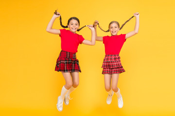 Playing together. happy children on yellow wall. childhood happiness. trendy school uniform. funny jump. red fashion girls. english style fashion. happy little girls in checkered skirt. beauty look