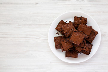 Homemade chocolate brownies on a white plate on a white wooden table, top view. Flat lay, overhead, from above. Copy space.