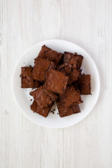 Homemade chocolate brownies on a white plate on a white wooden background, top view. Flat lay, overhead, from above. Closeup.