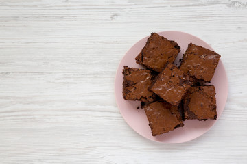 Homemade chocolate brownies on a pink plate on a white wooden background, top view. Flat lay, overhead, from above. Copy space.