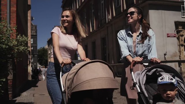 young happy mothers women with baby strollers walk down the street talking walk