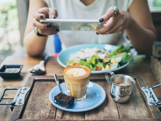 Woman's hands taking photo of coffee cup on wooden table by smartphone