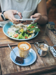 Woman's hands taking photo of coffee cup on wooden table by smartphone