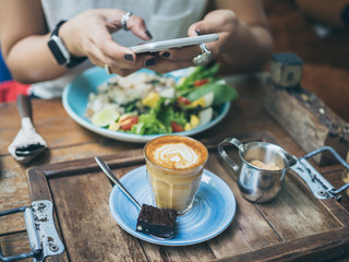 Woman's hands taking photo of coffee cup on wooden table by smartphone
