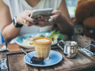 Woman's hands taking photo of coffee cup on wooden table by smartphone