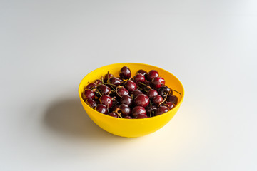 Ripe juicy red cherries in a yellow bowl in the center on white table. Vitamin healthy food for a healthy lifestyle. 