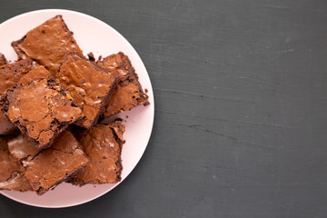 Homemade chocolate brownies on a pink plate on a black surface, top view. From above, overhead,...