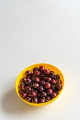 Ripe juicy red cherries in a yellow bowl  on white table. Vitamin healthy food for a healthy lifestyle. Vertical