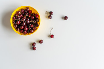 Top view. Ripe juicy red cherries in a yellow bowl on the left on white table. Vitamin healthy food for a healthy lifestyle. 