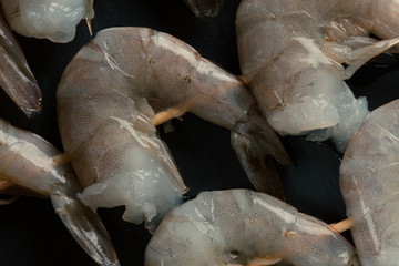 Uncooked shrimp skewers on black background