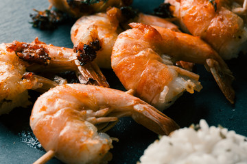 Headless fried prawns on wooden stick on black background