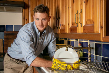 Unhappy handsome young man washing dishes in kitchen