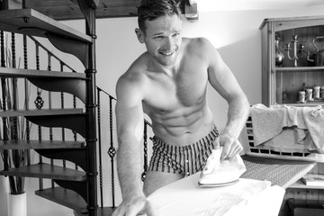 Man in his underwear with six pack abs ironing clothes  and smiling