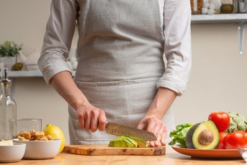 Cooking. Chef slices avocado, in the process of vegetarian salad in the home kitchen. Light background. Restaurant menu, menu, recipe book. Healthy nutrition, detox