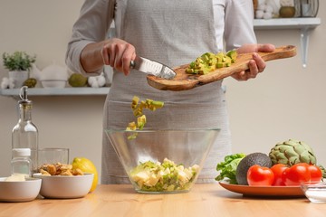 Cooking. The chef pours avocado, in the process of a vegetarian salad in the home kitchen. Light background. Restaurant menu, menu, recipe book. Healthy nutrition, detox