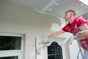 plasterer in red shirt works on white plaster of old house