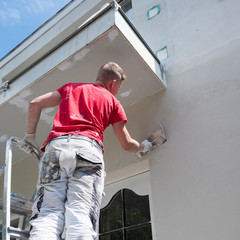 plasterer in red shirt works on white plaster of old house