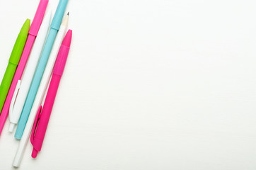 Multicolored bright school children pens and pencils on a white wooden background, school desk. Copy space, top view, flat lay.