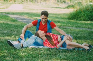 young couple in love is sitting on a blanket in the park, the girl is lying on the guy's lap and talking. Picnic for couples in love.