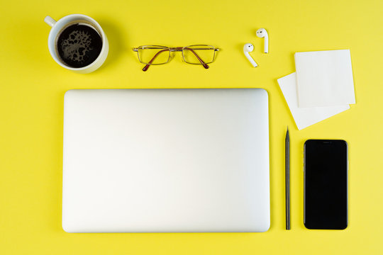 Laptop Phone Glasses Yellow Minimal Object Flat Lay. Smartphone Airpod on Freelance Business Table Background. Blank Corporate Workplace Inspiration with Coffee Cup Simple Deadline Concept Top View