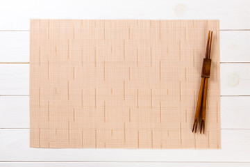 two sushi chopsticks with empty brown bamboo mat or wood plate on white wooden Background Top view with copy space. empty asian food background