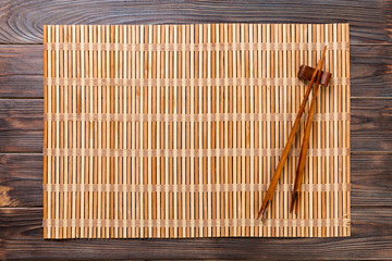 two sushi chopsticks with empty brown bamboo mat or wood plate on wooden Background Top view with copy space. empty asian food background