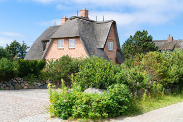 Fototapeta na wymiar Typical house with straw roof in small village on Sylt island, Germany.