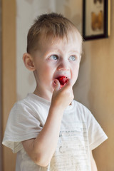a boy of three years in a Sunny kitchen eating ripe red strawberries
