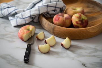 Plattpfirsiche mit Messer und Geschirrtuch in Holz Schale auf Küchen Marmor Tisch