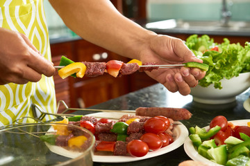 Close-up of man holding skewer with raw meat and fresh vegetables and preparing kebab for barbecue
