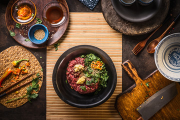 Mincemeat in black bowl with chopped garlic, chili, ginger and herbs on dark kitchen table background with sesame and soy sauce in bowls, top view. Stuffing or meat balls preparation. Asian cuisine