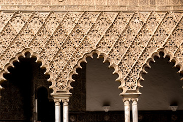 Arches and columns from the Real Alcazar of Sevilla, Spain with intricate hand carved geometric patterns.
