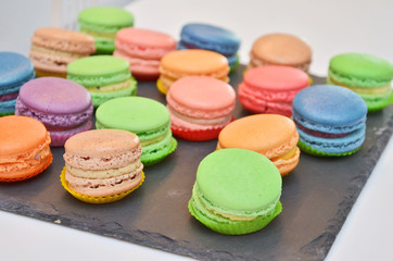 Fototapeta na wymiar Different types of sweet colored macarons pastry on a black stone plate at a banquet