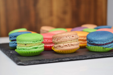 Different types of sweet different colored macarons pastry on a black stone plate at a banquet on wooden background