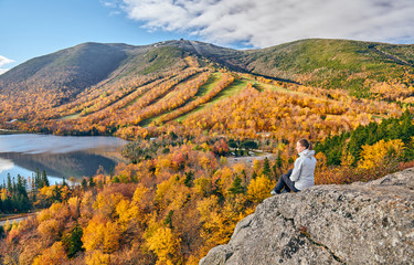 Woman hiking at Artist's Bluff in autumn. View of Echo Lake. Fall colours in Franconia Notch State Park. White Mountain National Forest, New Hampshire, USA