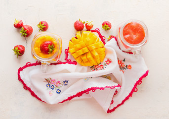 Glass jars with strawberries and mango smoothies on white table background, top view. Healthy fruits and berries breakfast