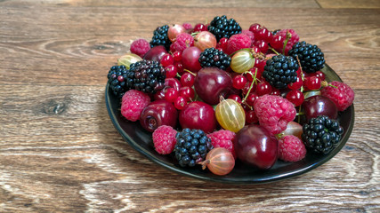 Fototapeta na wymiar Colorful photo of berries on the plate on the wooden surface (blackberry, cherry, gooseberry, raspberry, redcurrant)