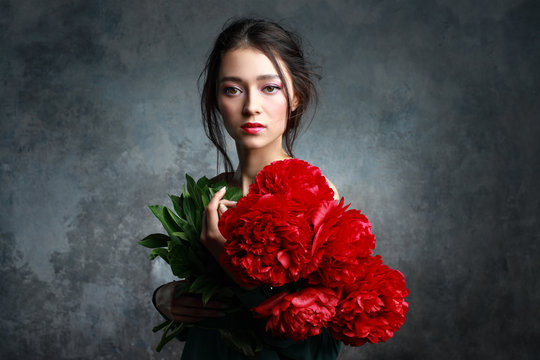 Beautiful girl in tender green dress with bouquet flowers peonies in hands. Playful fashion model looking at camera