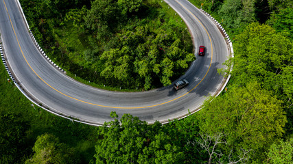 Aerial view over tropical tree forest with a road going through with car, Forest Road.