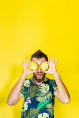 Young bearded man holding slices of pineapple in front of his eyes, surprised