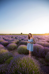 Young, beautiful, pretty girl with tattoos in a dress. Woman standing among blooming colorful flowers in a lavender field during a warm summer sunset.