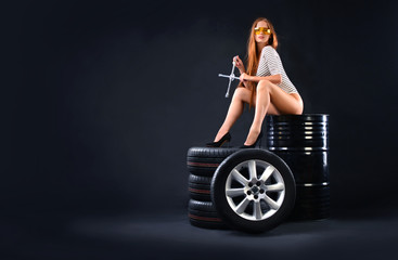 Tires and girl. Sexy girl sitting on tires. She holds wheel wrench in her hands. Auto service...