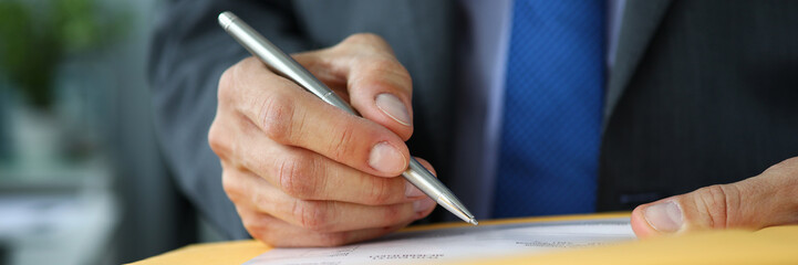Male clerk in suit and tie at workplace hold in hands silver pen filling out application form