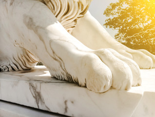 white sculpture close-up of marble powerful paw of a lion on a pedestal in the sunlight