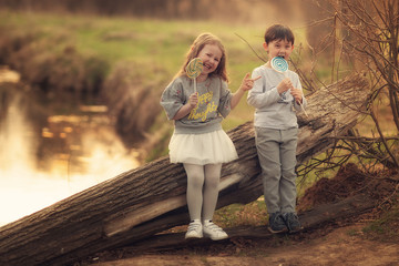 children leaning on the old log in the park eating lollipops