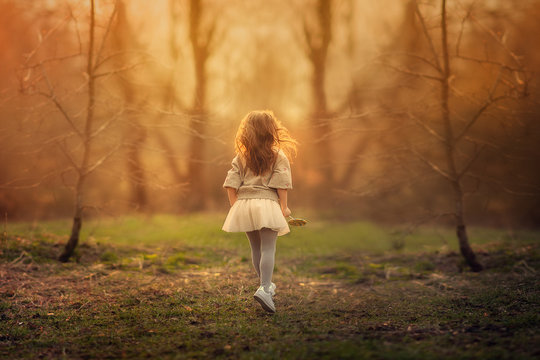 Back View Of Small Girl Standing In The Spring Park Between The Trees