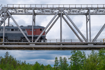 cargo tanker train crossing steel bridge in low view under blue sky on a summer day.
